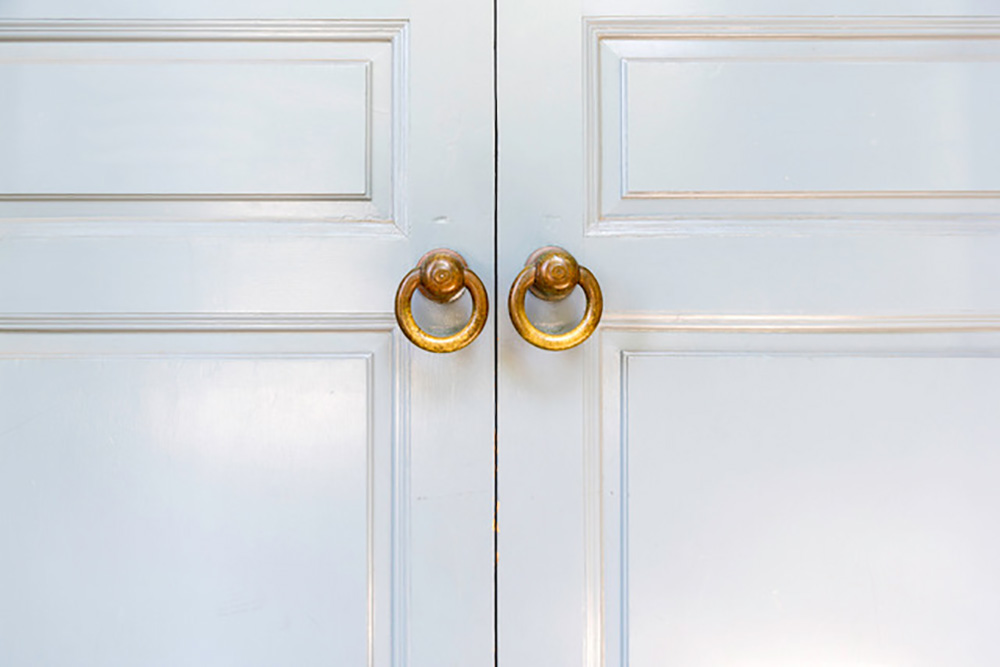 closeup of two plain white wooden doors with two small, circular brass doorknobs